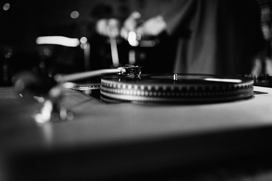 Black-and-white close-up of a turntable with the tonearm cued over a spinning record.